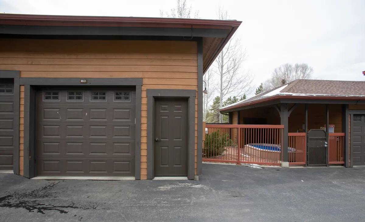 An exterior shot showcasing the heated private garage doors alongside the condo's entryway and a fenced-in area. The scene includes spaces for parking vehicles and easy access for unloading, all with a welcoming, family-friendly vibe.