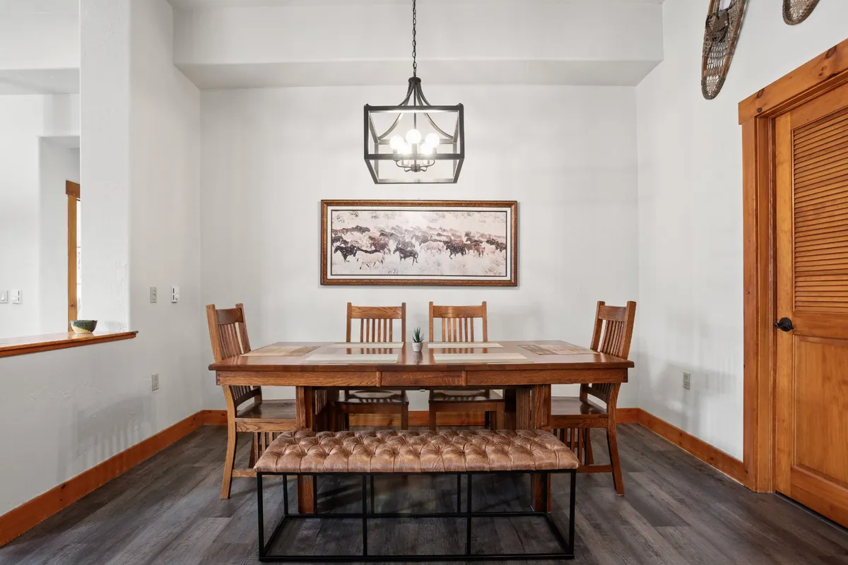 A welcoming dining area with a large table, chandelier overhead, stylish wall art, and bench seating. The scene is set for family meals, board games, or festive celebrations, emphasizing the lively communal aspect of the open-concept space.