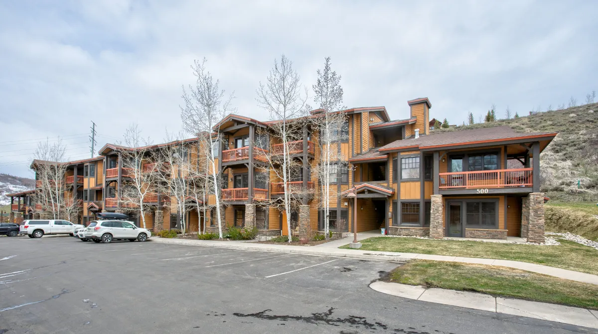 This image features the building's exterior facade with balconies overlooking surrounding greenery and natural landscapes. The scene is bright and welcoming, suggesting easy access to outdoor spaces and nearby nature trails. The architecture is inviting and family-friendly, with areas that feel both private and connected to the outdoors.