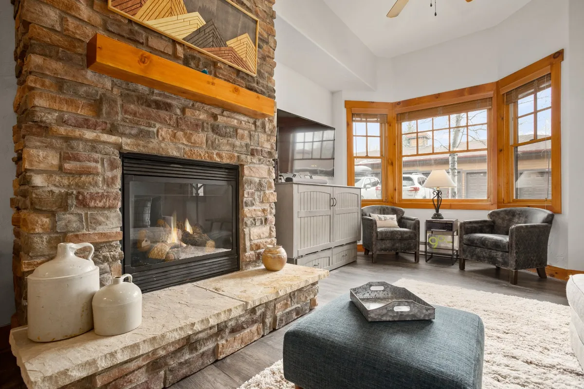 A cozy interior with a stone fireplace, comfortable seating, and large bay windows, inviting guests to unwind or work in a warm, welcoming atmosphere while still feeling connected to the scenic exterior.